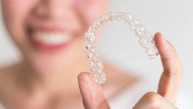 A person holding up a clear dental retainer with their hand.