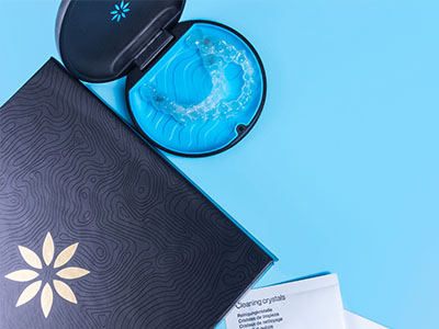 The image shows a product with a blue lid placed next to an open box on a light blue background, featuring a design that resembles a stylized flower or sunburst pattern.