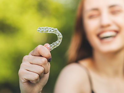 A smiling woman holds up an oversized toothbrush prop with a playful expression.