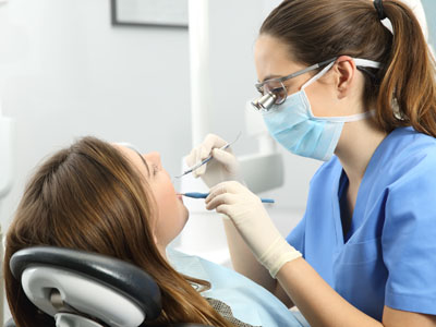 A dental hygienist is performing a teeth cleaning procedure on a patient while wearing full personal protective equipment  PPE , including gloves, goggles, and a face mask.