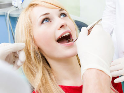 A woman receiving dental care with a dentist performing a procedure, while another person observes.