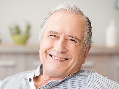 The image shows an elderly man with gray hair, wearing glasses and a blue shirt, sitting comfortably with his eyes closed and smiling slightly, appearing content and relaxed.