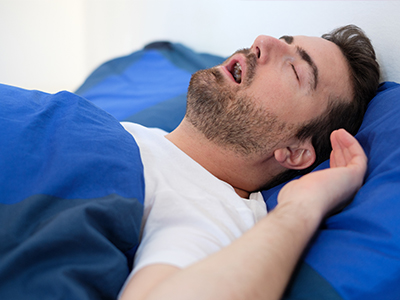 A man sleeping peacefully on a bed with his mouth open.